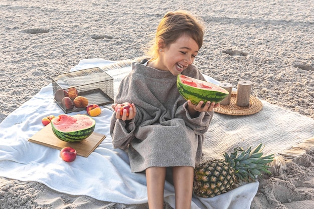 Little girl on the sandy seashore at a picnic with fruits