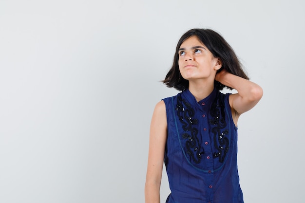 Little girl scratching head in blue blouse and looking hesitant.