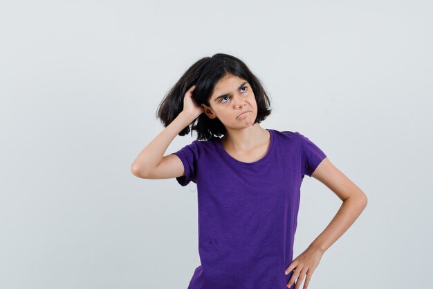 Little girl scratching head in t-shirt and looking hesitant.