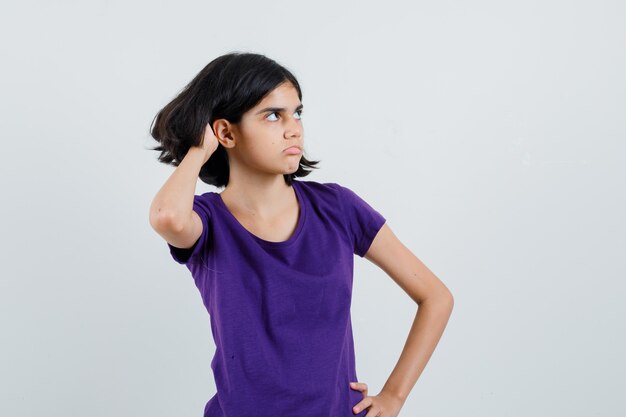 Little girl scratching head in t-shirt and looking hesitant