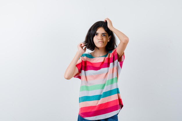 Little girl scratching head in t-shirt and looking thoughtful , front view.