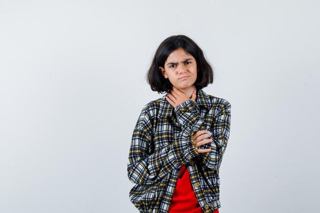 Little girl in shirt,jacket holding hand on throat and looking painful , front view.