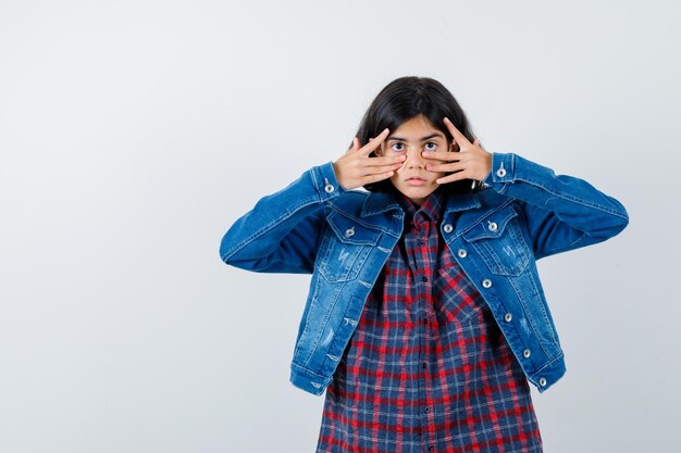 Little girl in shirt, jacket looking through fingers and looking puzzled , front view.