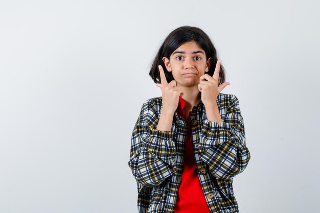 Little girl in shirt,jacket pointing up and looking assured , front view.