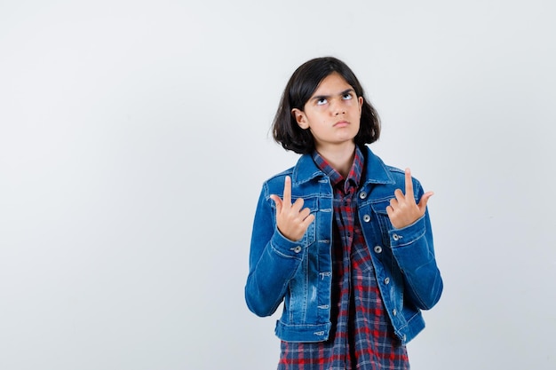 Little girl in shirt, jacket pointing up and looking indecisive , front view.