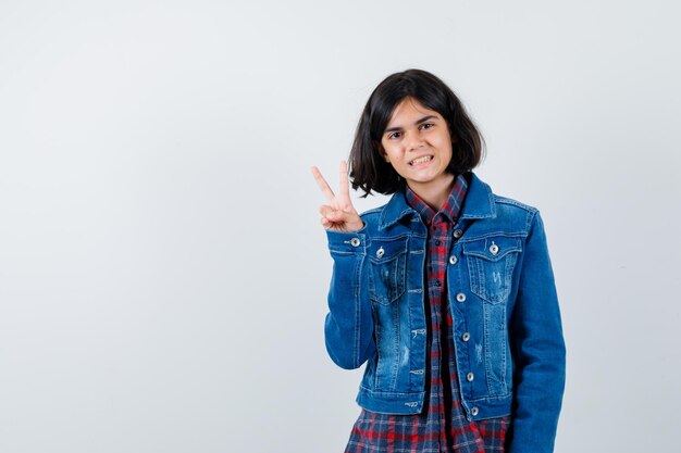 Little girl in shirt, jacket showing V-sign and looking confident , front view.