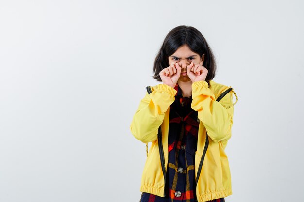 Маленькая девочка показывает жест плача руками в клетчатой рубашке, куртке и задумчиво