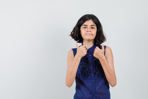 Little girl showing double thumbs up, curving lips in blue blouse