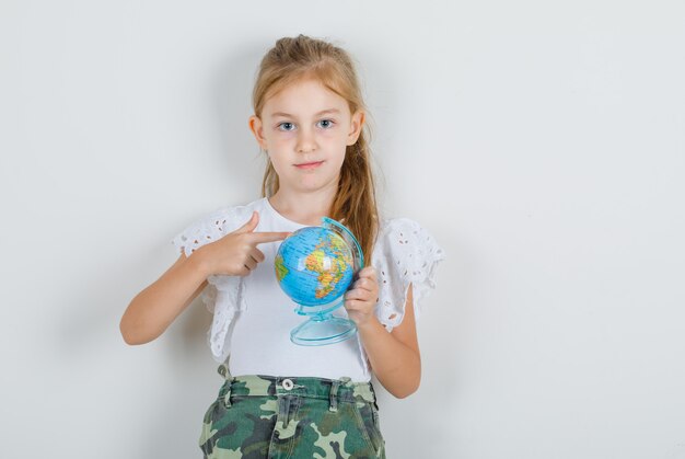 Little girl showing globe with finger in white t-shirt