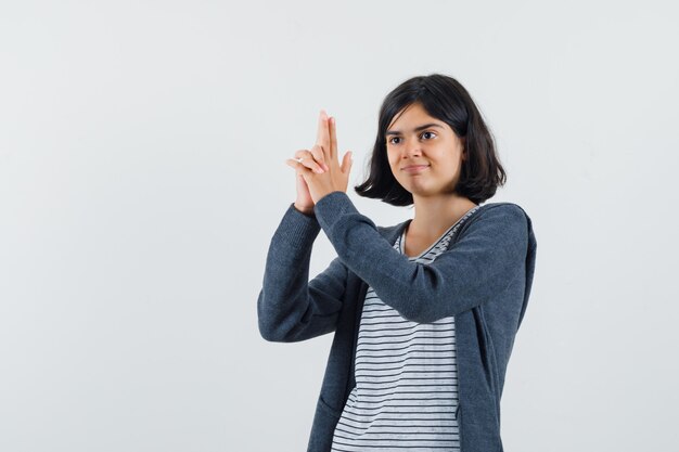 Tシャツ、ジャケットで銃のジェスチャーを示し、自信を持って見える少女。