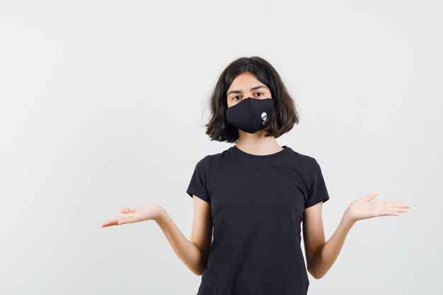 Free photo little girl showing helpless gesture in black t-shirt, mask front view.