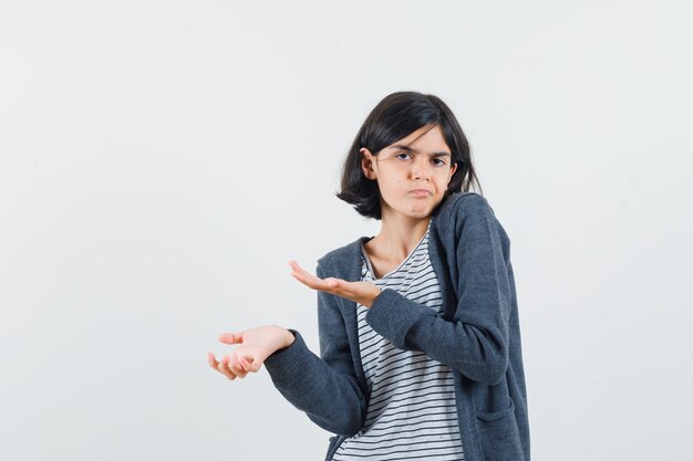 Little girl showing helpless gesture by shrugging in t-shirt, jacket and looking confused.