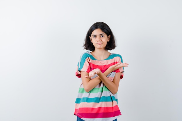 Маленькая девочка показывает беспомощный жест в футболке и выглядит смущенным, вид спереди.