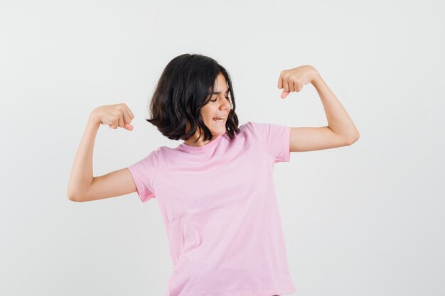 Little girl showing muscles of arms in pink t-shirt and looking confident. front view.