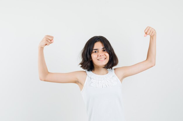 Little girl showing muscles of arms in white blouse and looking happy , front view.