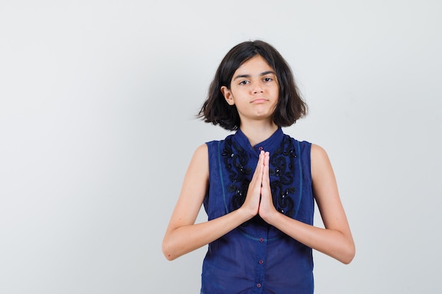 Foto gratuita bambina che mostra il gesto di namaste in camicetta blu e che sembra sicura