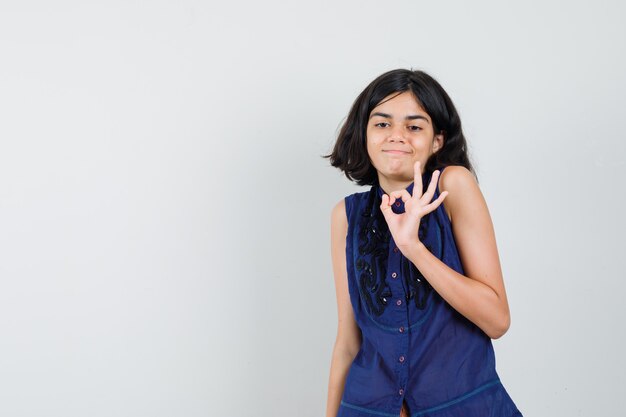 Little girl showing ok gesture by shrugging in blue blouse