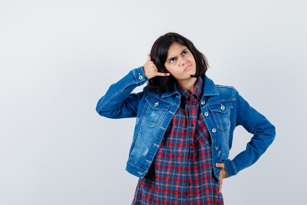 Little girl showing phone gesture in shirt, jacket and looking thoughtful. front view.