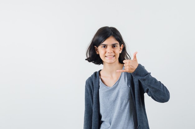 Little girl showing phone gesture in t-shirt, jacket and looking helpful