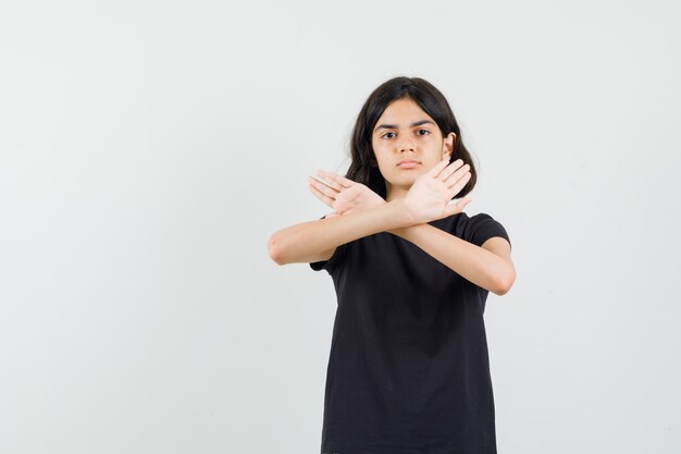 Little girl showing refusal gesture in black t-shirt and looking strict. front view.