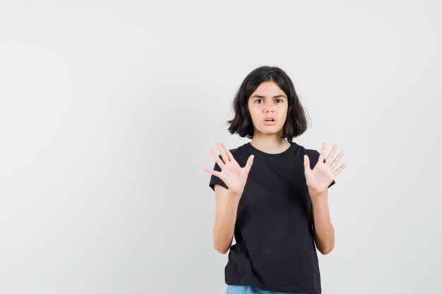 Little girl showing refusal gesture in black t-shirt, shorts and looking scared. front view.