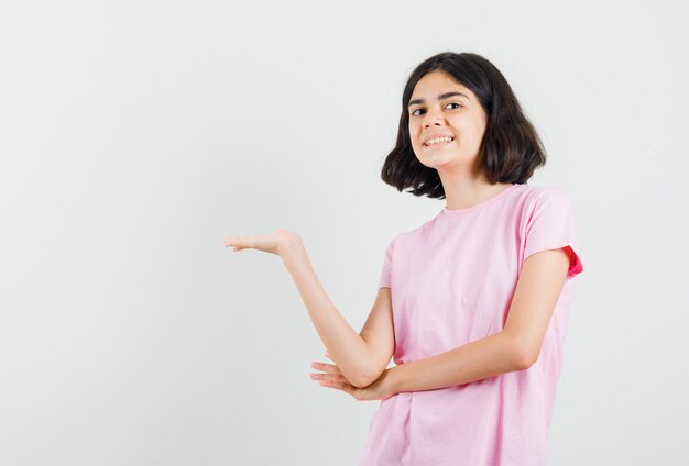 ピンクのTシャツで何かを見せたり、歓迎したり、陽気に見える少女、正面図。