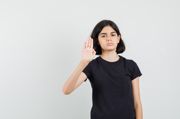 Маленькая девочка показывает жест остановки в черной футболке и выглядит раздраженным, вид спереди.