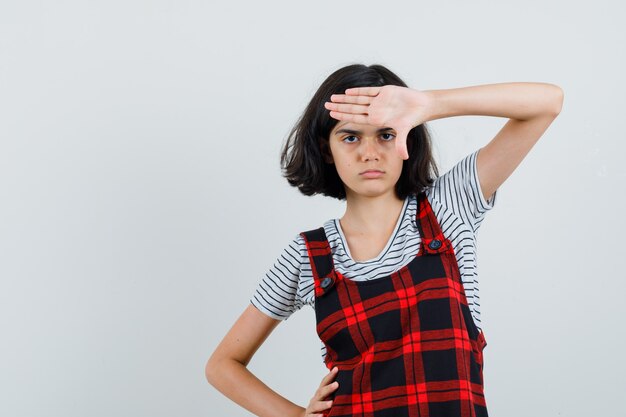 Free photo little girl showing stop gesture in pinafore dress and looking resolute