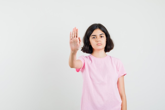 Маленькая девочка показывает жест остановки в розовой футболке и выглядит серьезно. передний план.