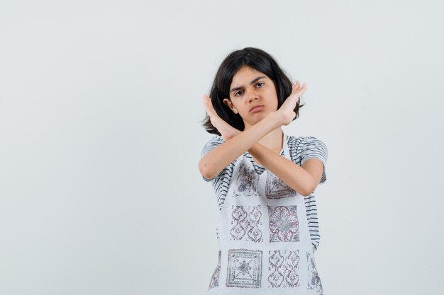 Little girl showing stop gesture in t-shirt, apron and looking annoyed