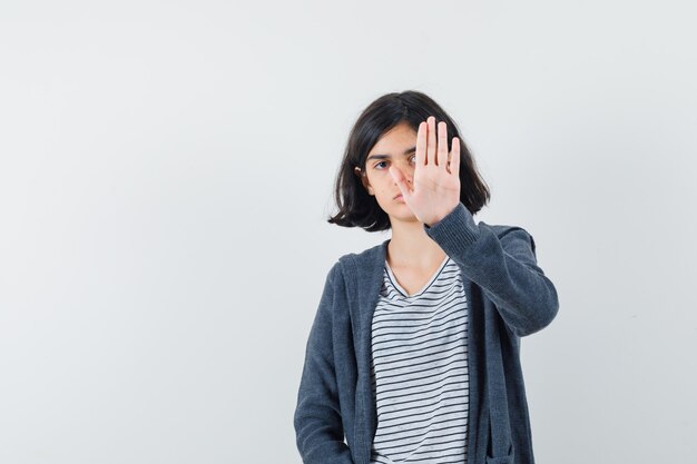 Little girl showing stop gesture in t-shirt, jacket and looking annoyed