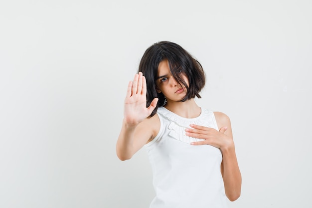 Little girl showing stop gesture in white blouse and looking serious. front view.