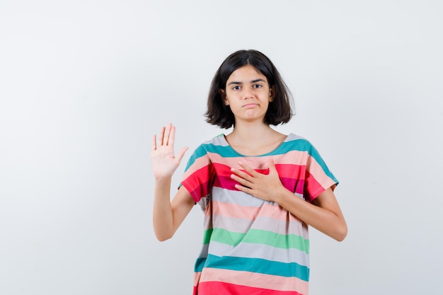 Little girl showing stop sign while holding hand on chest in t-shirt, jeans and looking displeased. front view.