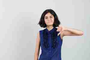 Free photo little girl showing thumb down in blue blouse and looking dissatisfied.