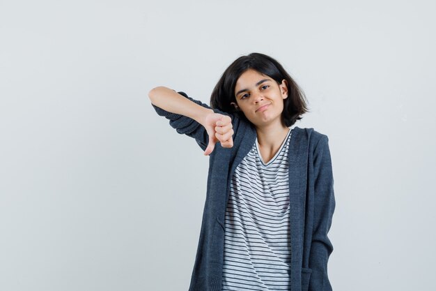 Tシャツ、ジャケットで親指を下に見せて不満を探している少女