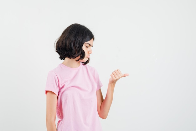 Little girl showing thumb middle in pink t-shirt and looking pensive , front view.