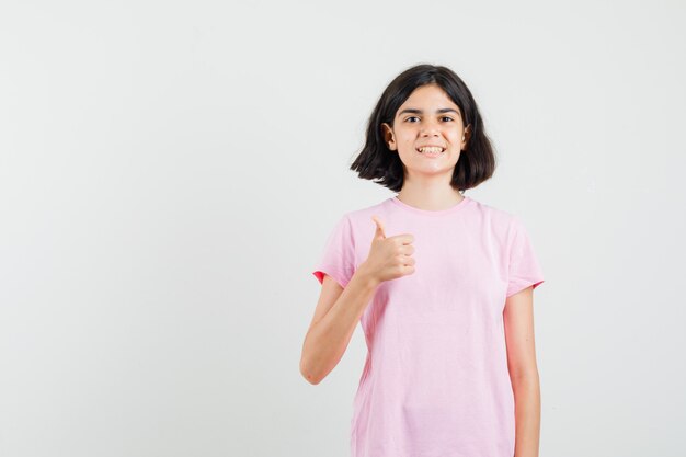 Little girl showing thumb up in pink t-shirt and looking glad. front view.