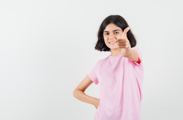 ピンクのTシャツを着て親指を立てて楽観的に見える少女。正面図。