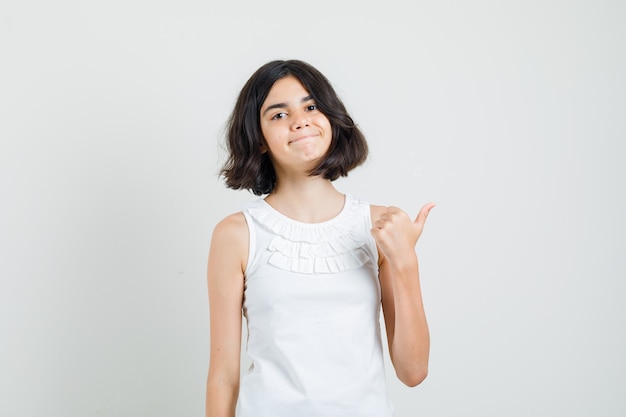 Little girl showing thumb up in white blouse and looking confident , front view.