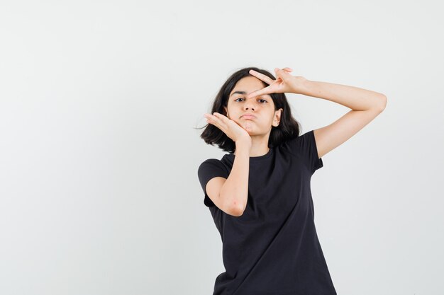 Little girl showing v-sign in black t-shirt and looking confident. front view.