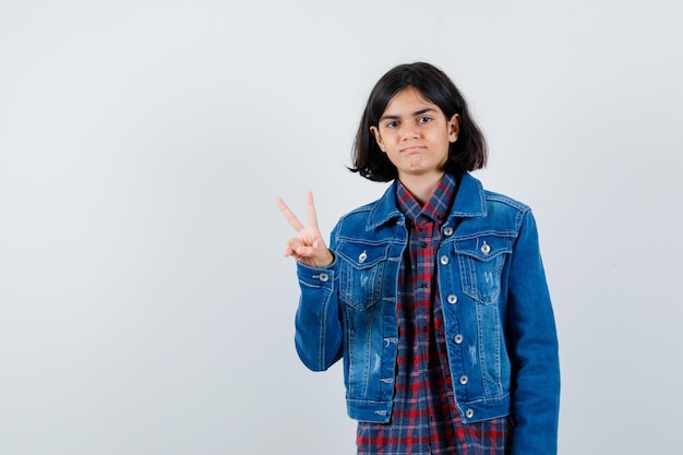 Little girl showing victory gesture in shirt, jacket and looking confident , front view.