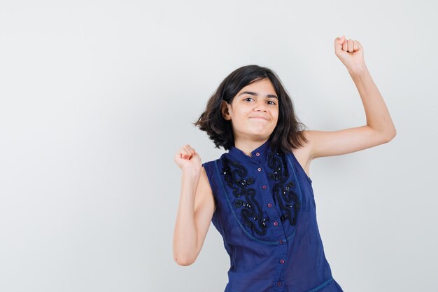 Little girl showing winner gesture in blue blouse and looking blissful.