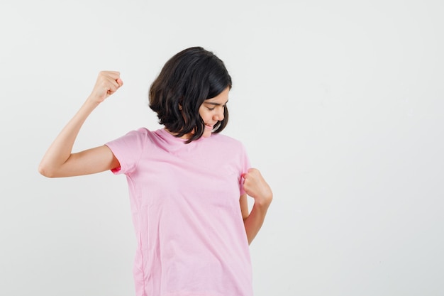 Little girl showing winner gesture in pink t-shirt and looking blissful , front view.