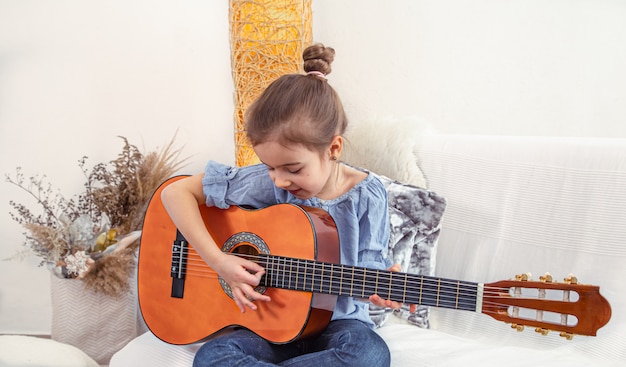 A little girl sits on the couch and plays the guitar