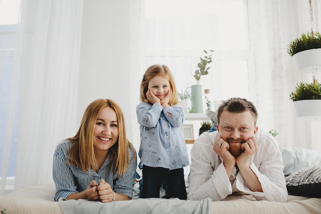 Little girl sits with her parents on a white bed in a bright room