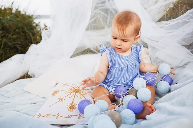 Little girl sits with a light garland under white tent