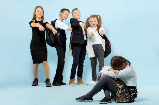 Free photo little girl sitting alone on floor and suffering an act of bullying while children mocking