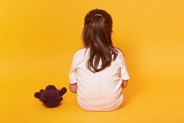 Little girl sitting backwards with brown teddy bear