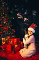 無料写真 クリスマスツリーのそばに座ってプレゼントを開梱する少女