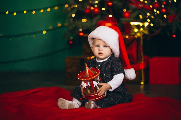 Little girl sitting by Christmas tree with toy